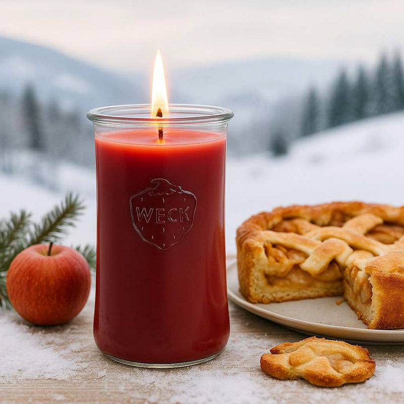 XXL-Duftkerze Apfeltraum Winteredition im WECK-Delikatessenglas neben frischem Apfelkuchen, auf schneebedecktem Tisch mit skandinavischer Winterlandschaft im Hintergrund