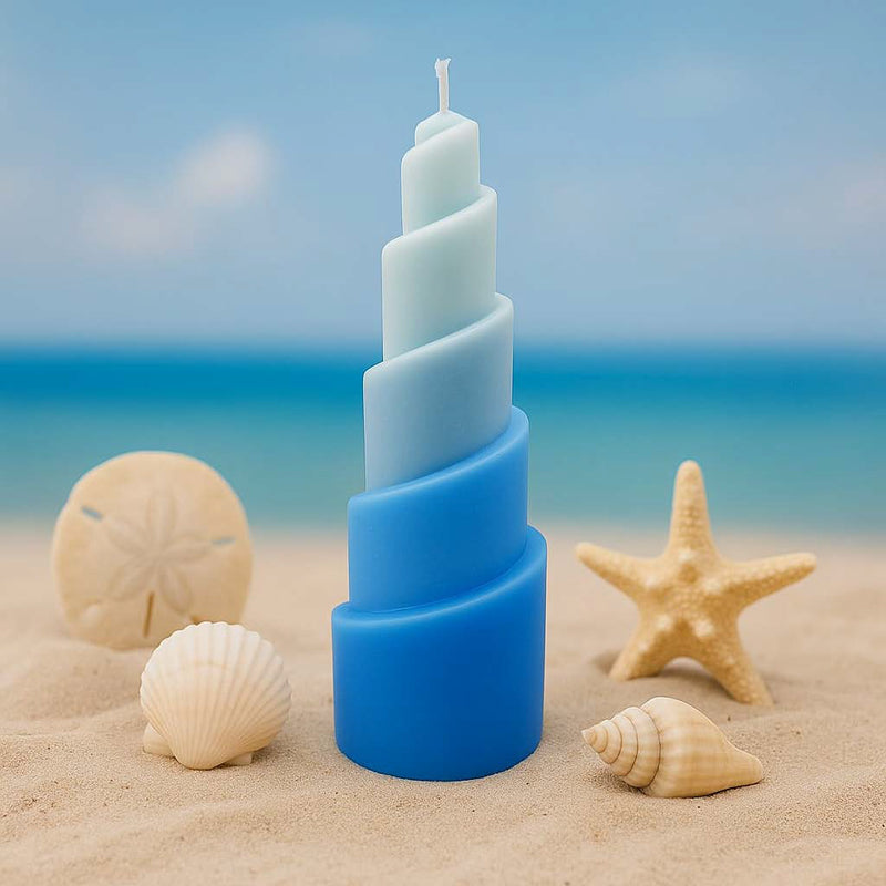 Spiralig gedrehte Kerze im maritimen Leuchtturm-Look, arrangiert mit Muscheln und Dekosteinen auf hellem Untergrund – moderne maritime Deko mit Rapswachskerze