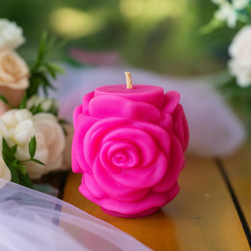 Romantische Stumpenkerze in Rosenform, handgegossen aus Rapswachs, dekorativ arrangiert mit Blumen im Hintergrund