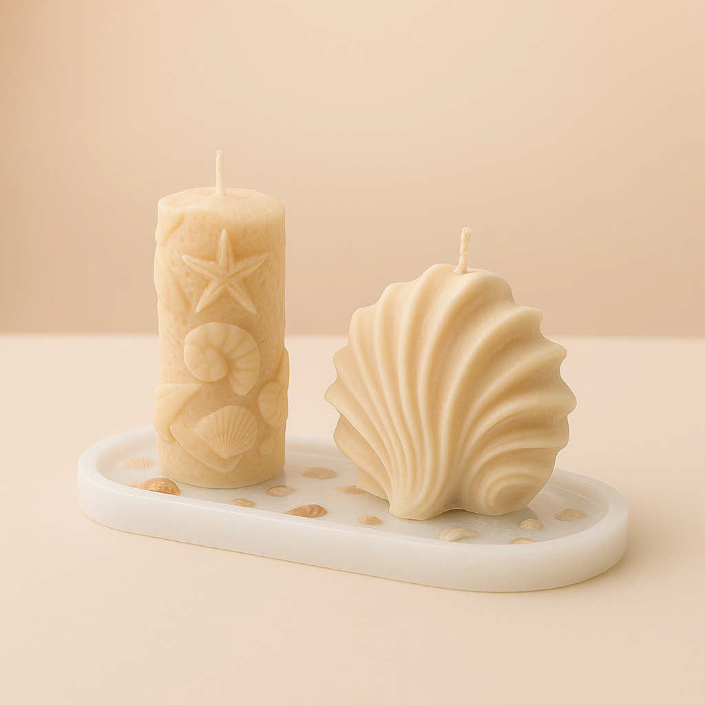 Zwei beige Kerzen in Meeresform – eine Muschelkerze und eine Stumpenkerze mit Seestern- und Muscheldetails – stehen auf einem sechseckigen, kleegrünen Epoxidharz-Untersetzer. Die Komposition vermittelt maritimes Flair und stilvolle Natürlichkeit.