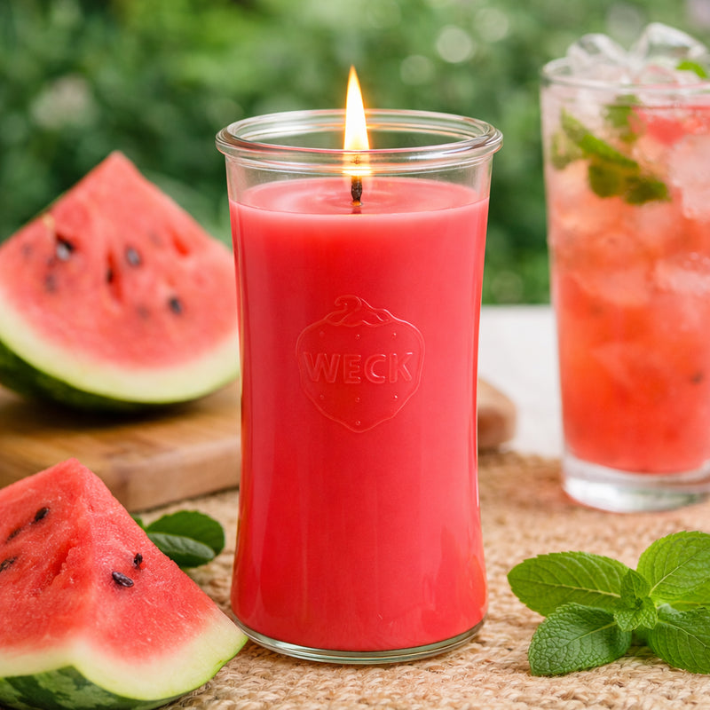 Brennende rote Duftkerze im WECK-Glas auf Naturmatte, umgeben von frischen Wassermelonenstücken, Minzblättern und einem Glas Wassermelonendrink – sommerliche Szene für die Duftkerze Wassermelonensorbet.