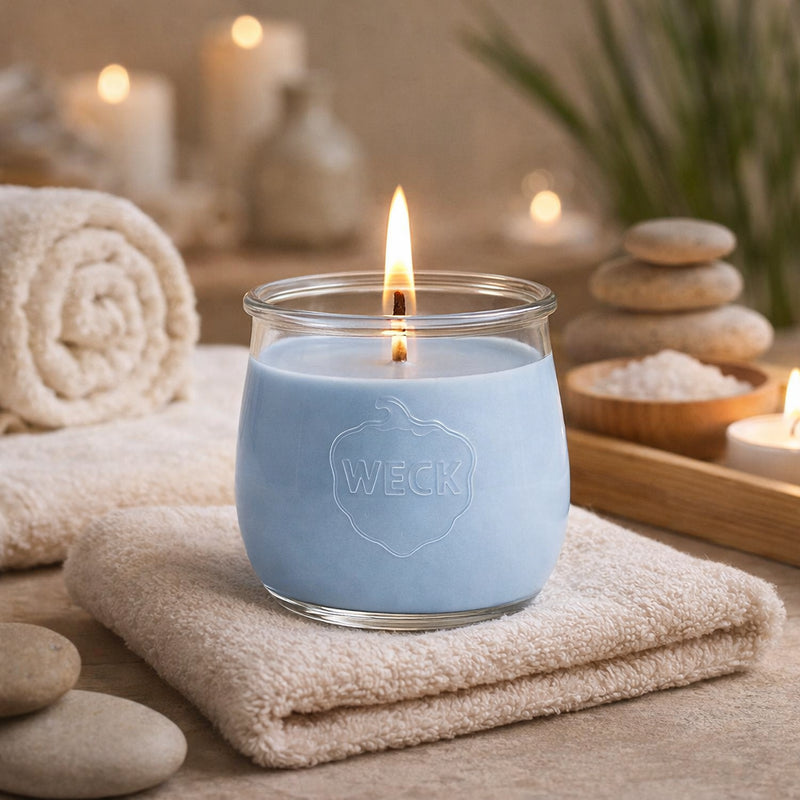 Duftkerze Wellnessmoment im WECK-Glas auf weichem Handtuch, umgeben von Natursteinen, Teelichtern und Spa-Accessoires – stimmungsvolle Szene in entspannter Wohlfühlatmosphäre
