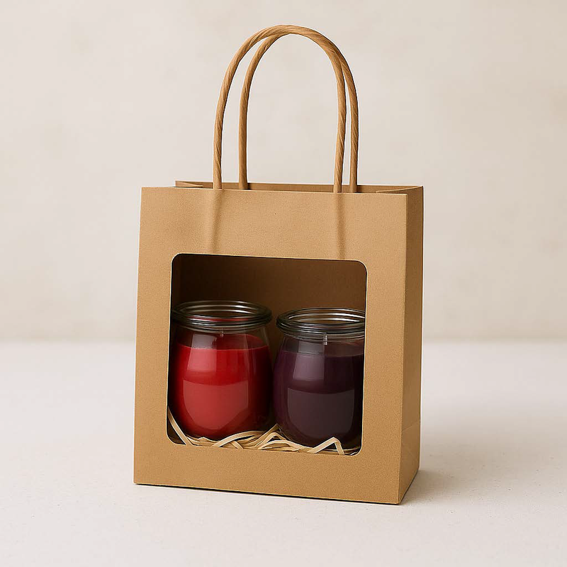 Zwei Mini-Duftkerzen in winterlichen Farben (rot & dunkelviolett) in einer Kraftpapier-Geschenktüte mit Sichtfenster und Füllmaterial aus Holzwolle.