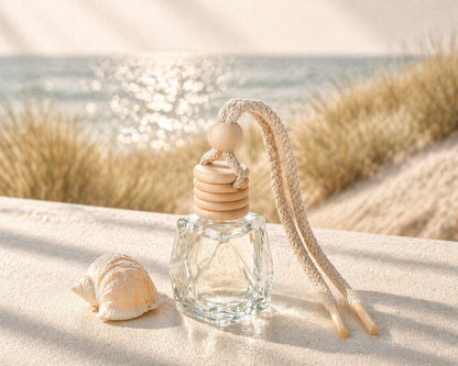 Autoduft Samtige Brise aus Glas mit Holzdeckel auf Sand neben einer Muschel mit Meer im Hintergrund in heller, ruhiger Atmosphäre