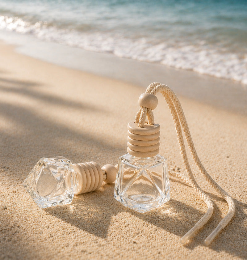 Autoduft Anhänger aus Glas mit Holzdeckel und Kordel im Sand am Strand, mit Meer im Hintergrund bei warmem Licht