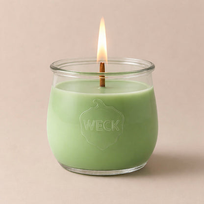 Duftkerze aus Pflanzenwachs im klaren WECK-Glas mit pastellgrünem Wachs und brennendem Docht vor neutralem Hintergrund.