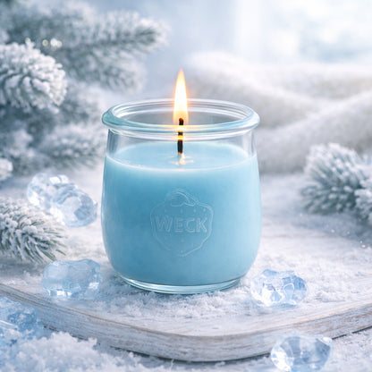 Helle Duftkerze in eisblauem Wachs, brennend im WECK-Glas, auf verschneitem Holztablett mit Eiskristallen und frostbedeckten Tannenzweigen – stimmungsvolles Winterbild mit frischer, klarer Atmosphäre.