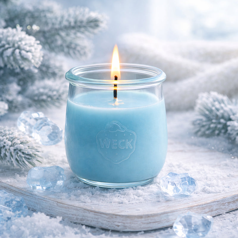 Helle Duftkerze in eisblauem Wachs, brennend im WECK-Glas, auf verschneitem Holztablett mit Eiskristallen und frostbedeckten Tannenzweigen – stimmungsvolles Winterbild mit frischer, klarer Atmosphäre.