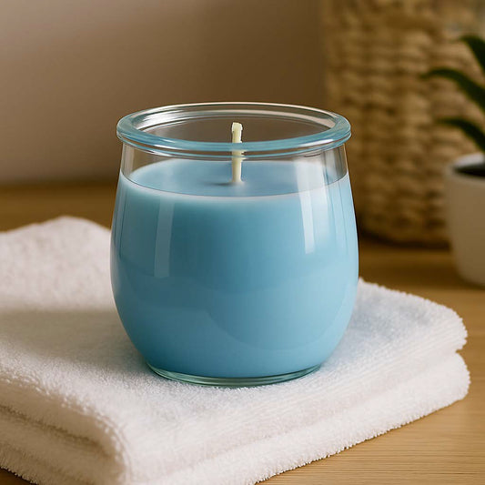 Eine hellblaue Duftkerze im XL-Weckglas von Candle Deko, brennend auf einem hellen Tisch mit weichem Tageslicht. Im Hintergrund eine gefaltete, weiße Textilie – symbolisiert den frischen, sauberen Duft von frisch gewaschener Wäsche. Die Szene vermittelt Ruhe, Ordnung und Reinheit