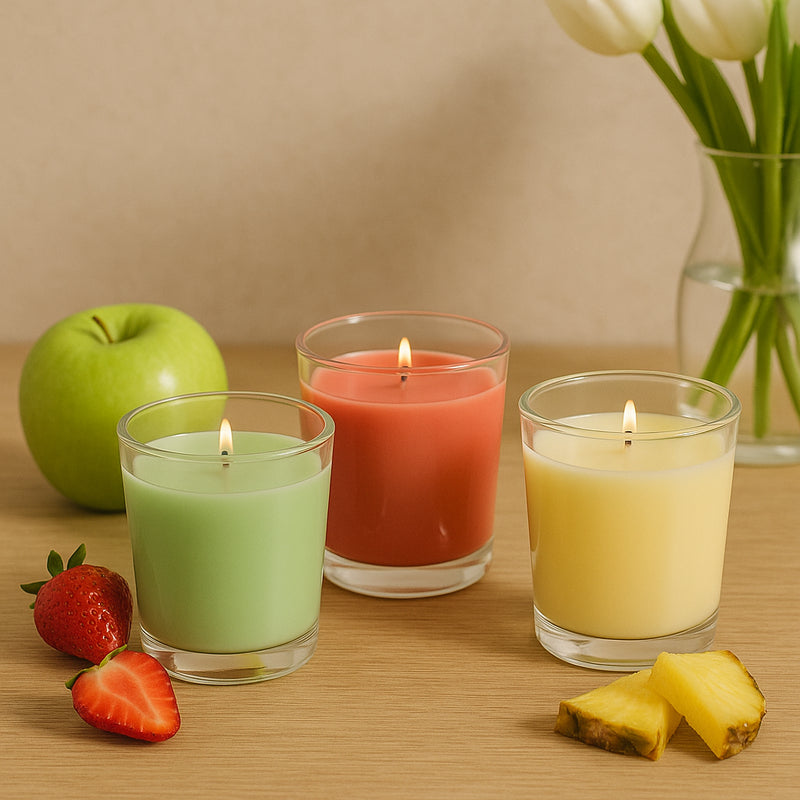 Drei brennende Duftkerzen im Tulpenglas in Apfelgrün, Erdbeerrot und Ananasgelb auf Holzoberfläche, dekoriert mit frischen Früchten und Tulpen – DuftSet Fruchtige Leichtigkeit.