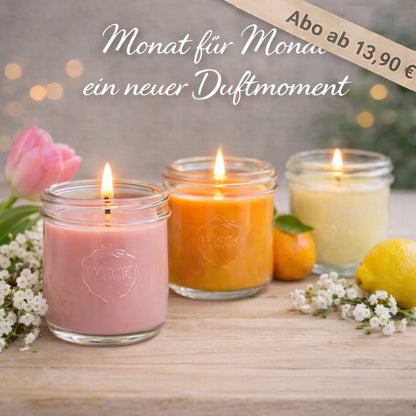 Drei brennende Duftkerzen im WECK-Glas auf einem Holztisch, symbolisch für die Duftreise im Abo. Im Vordergrund eine violette Kerze (Januar), daneben eine orangefarbene (Februar) und eine cremefarbene (März). Umgeben von Zitrusfrüchten, Blüten und Kraftpapier-Kärtchen mit Monatsnamen. Darüber der Schriftzug: „Monat für Monat ein neuer Duftmoment“.