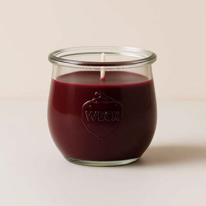 Brennende dunkelrote Duftkerze „Kaminfeuer Klassik“ im WECK-Glas mit Baumwolldocht vor beigem Hintergrund.