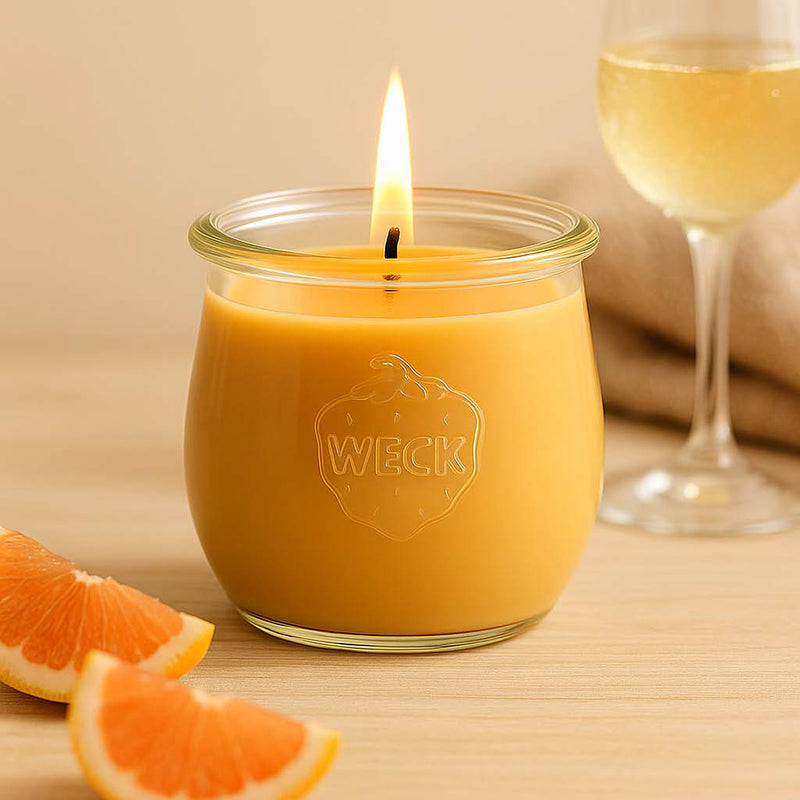 Pomelozauber Duftkerze brennend im WECK-Glas auf hellem Holz, dekoriert mit Grapefruitstücken und Sektglas. Frischer, fruchtiger Look im warmen Licht.