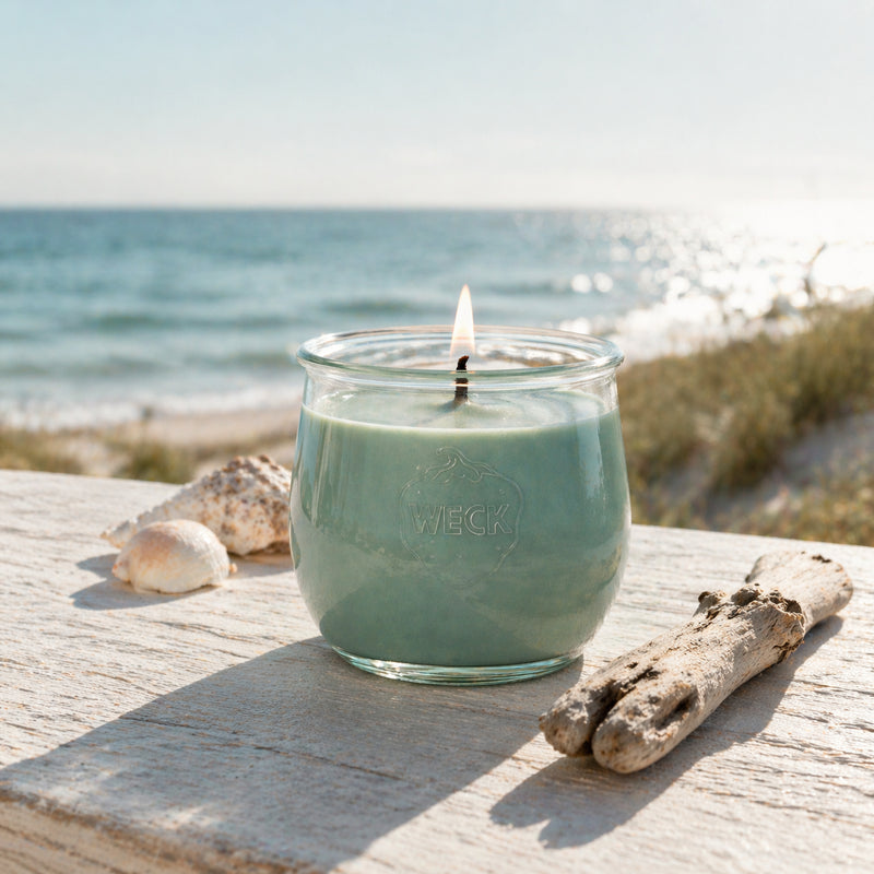 Samtige Brise Duftkerze im WECK-Glas auf hellem Holz am Meer, natürliches Licht, maritimes Lifestyle-Bild mit Muscheln und Treibholz