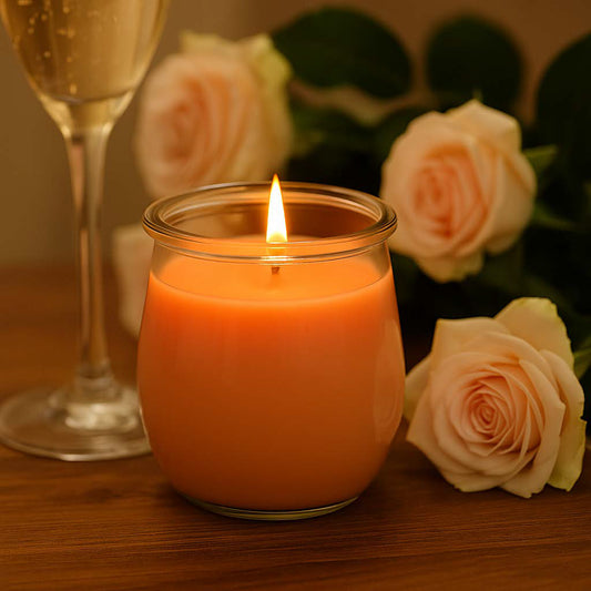 Zart pfirsichfarbene Duftkerze in elegantem Glas, angezündet neben Rosen und Schaumwein in festlicher Atmosphäre – stimmungsvolles Bild für besondere Momente