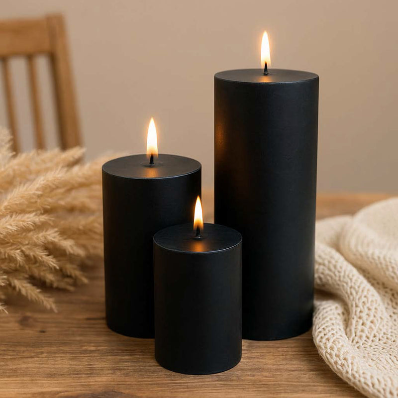 Drei schwarze Stumpenkerzen auf einem Tisch mit dunkler Dekoration – elegantes Wohnaccessoire im minimalistischen Stil.