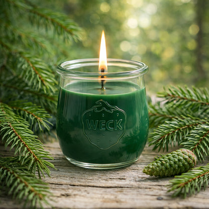 Tannenbaum-Duftkerze im Weckglas – grün, brennend, auf Holz mit Tannennadeln – stimmungsvolles Naturbild für ganzjährige Verwendung.
