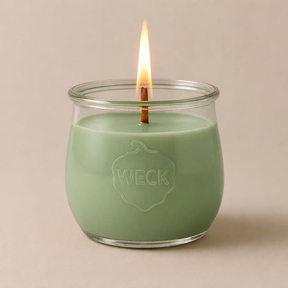 Salbeigrüne Duftkerze Teeoase im WECK-Glas mit Holzdocht, vor neutralem Hintergrund. Pflanzliches Wachs, klare Form, ruhiges Licht.