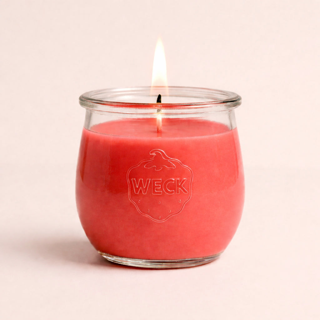Brennende Duftkerze in kräftigem Pink im WECK-Glas mit geprägtem Logo, zentriert vor warmem, neutralem Hintergrund – ruhige Studioaufnahme.