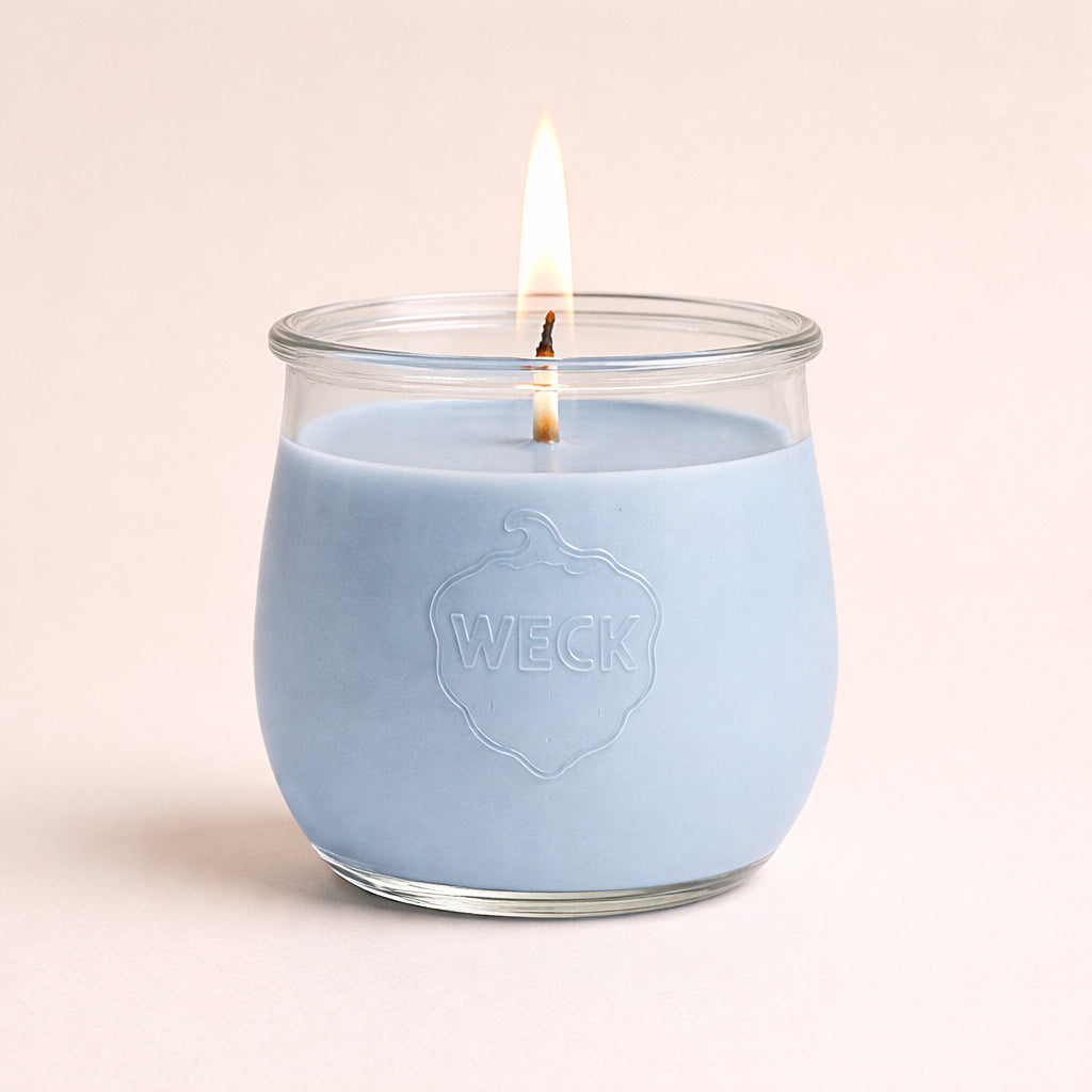 Brennende Duftkerze in zartem Babyblau im WECK-Glas mit geprägtem Logo, vor ruhigem Hintergrund  mit weichem Schatten – hochwertige Studioaufnahme.