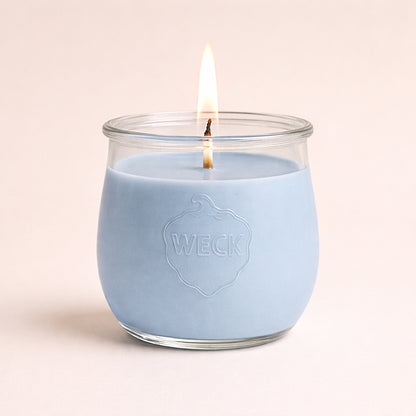 Brennende Duftkerze in zartem Babyblau im WECK-Glas mit geprägtem Logo, vor ruhigem Hintergrund  mit weichem Schatten – hochwertige Studioaufnahme.