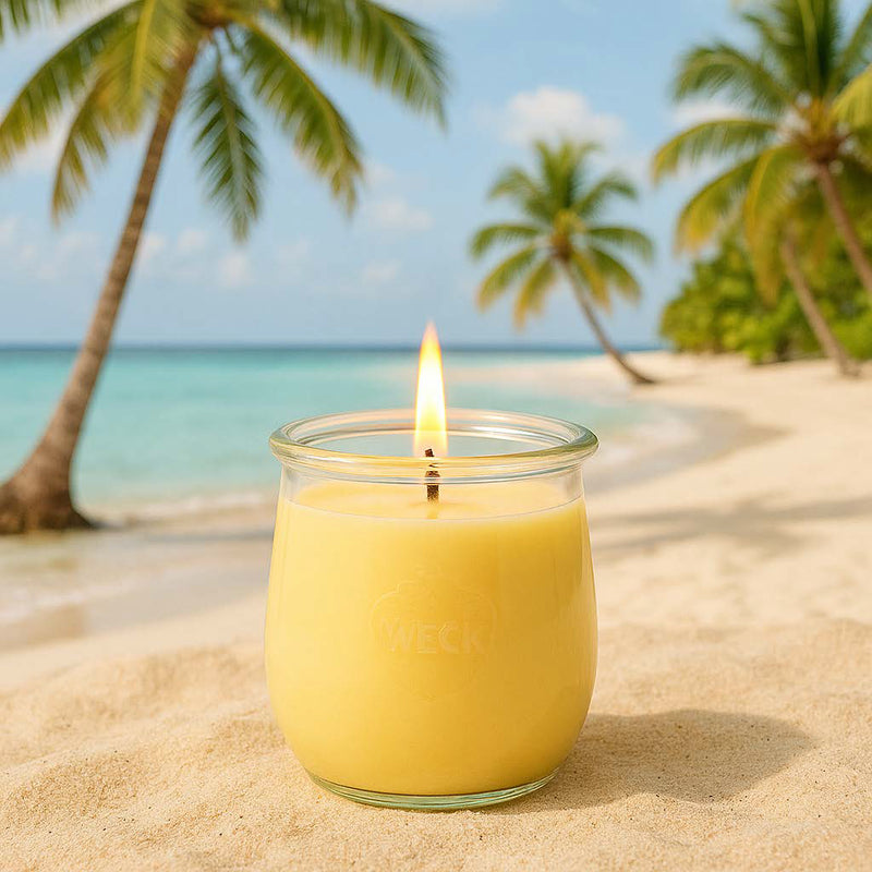 Große Ananas Duftkerze aus Kokoswachs im WECK-Tulpenglas im Sand vor Strand und Palmen.