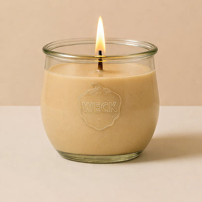 Brennende beige CandleDeko grosse Duftkerze im WECK-Tulpenglas vor neutralem Hintergrund.