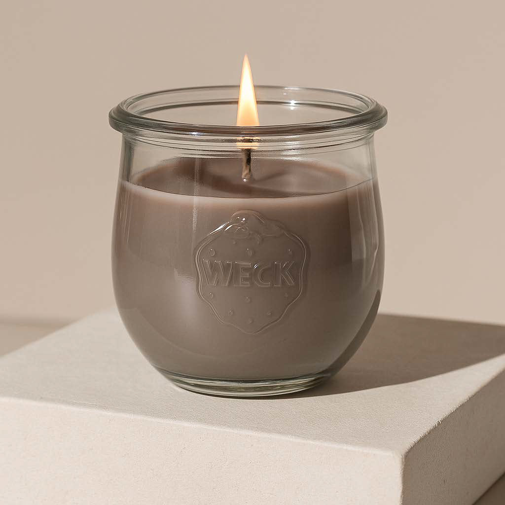 Große Duftkerze Nordische Küste aus Pflanzenwachs im klaren WECK-Glas mit taupefarbenem Wachs und brennender Flamme vor hellem neutralem Hintergrund.