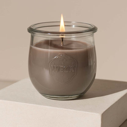 Große Duftkerze Nordische Küste aus Pflanzenwachs im klaren WECK-Glas mit taupefarbenem Wachs und brennender Flamme vor hellem neutralem Hintergrund.