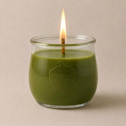 Brennende olivgruene CandleDeko grosse Duftkerze im WECK-Tulpenglas vor neutralem Hintergrund.