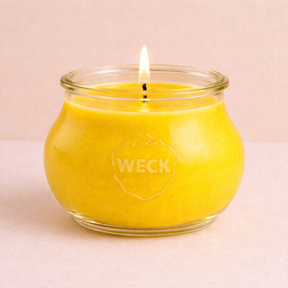 Brennende gelbe CandleDeko Grande Duftkerze im bauchigen, eleganten WECK-Glas vor neutralem Hintergrund.