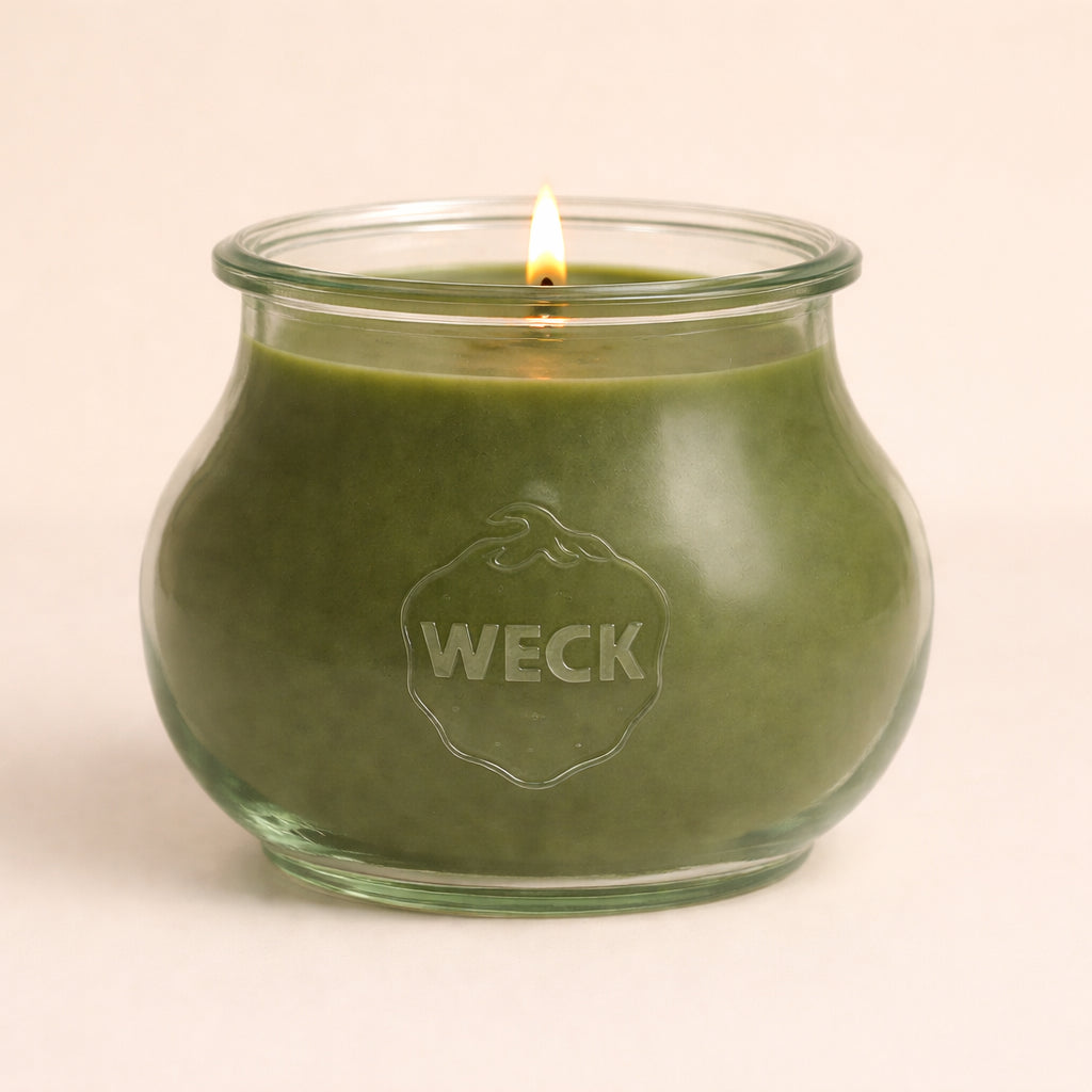 Brennende grüne CandleDeko Grande Duftkerze im bauchigen, eleganten WECK-Glas vor neutralem Hintergrund.