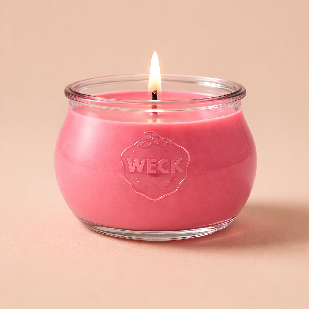 Brennende hellrote CandleDeko Grande Duftkerze im bauchigen, eleganten WECK-Glas vor neutralem Hintergrund.