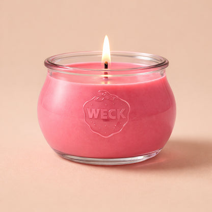Brennende hellrote CandleDeko Grande Duftkerze im bauchigen, eleganten WECK-Glas vor neutralem Hintergrund.