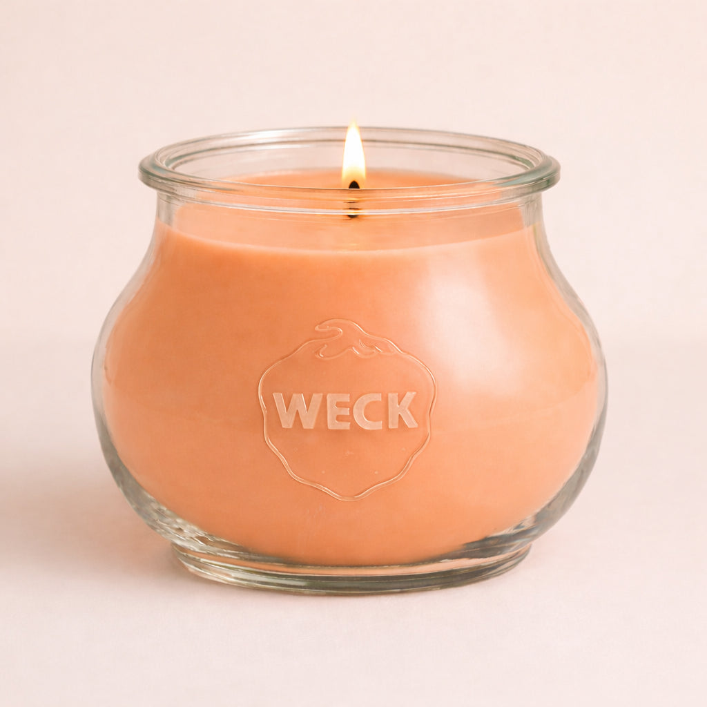 Brennende pfirsichfarbene CandleDeko Grande Duftkerze im bauchigen, eleganten WECK-Glas vor neutralem Hintergrund
