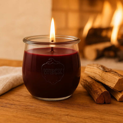 Große brennende dunkelrote CandleDeko Duftkerze im WECK-Glas auf Holztisch vor einem prasselnden Kaminfeuer.