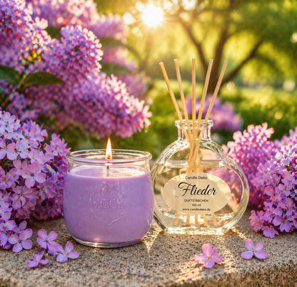 CandleDeko Duftkerzen & Raumduft Set Flieder mit brennender Pflanzenwachs-Duftkerze im WECK-Glas und Raumduft im Herzglas mit hellen Faserstäbchen zwischen lila Frühlingsblüten.