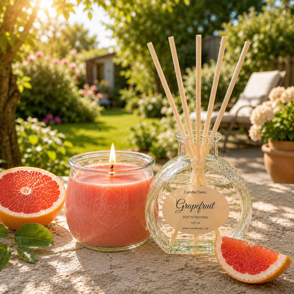 CandleDeko Duftdset Grapefruit mit brennender Pflanzenwachs-Duftkerze im WECK-Glas und Raumduft im Herzglas mit hellen Faserstäbchen zwischen frischen Grapefruitscheiben im Garten.