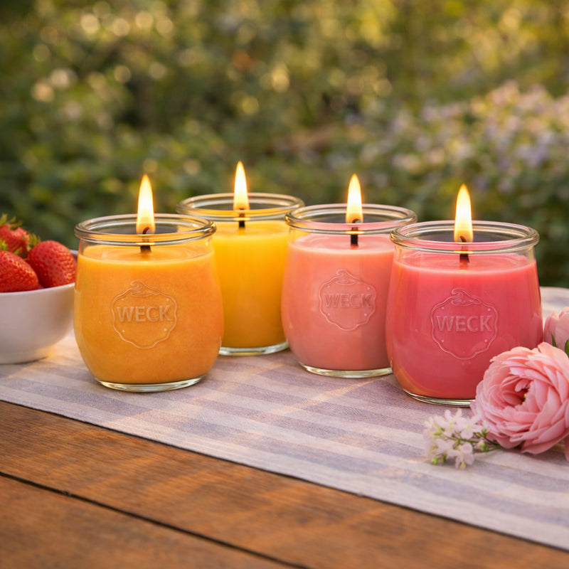 Großes CandleDeko Duftkerzen-Set mit vier brennenden bunten Kerzen aus pflanzlichem Kokoswachs im WECK-Glas neben frischen Erdbeeren im Garten.