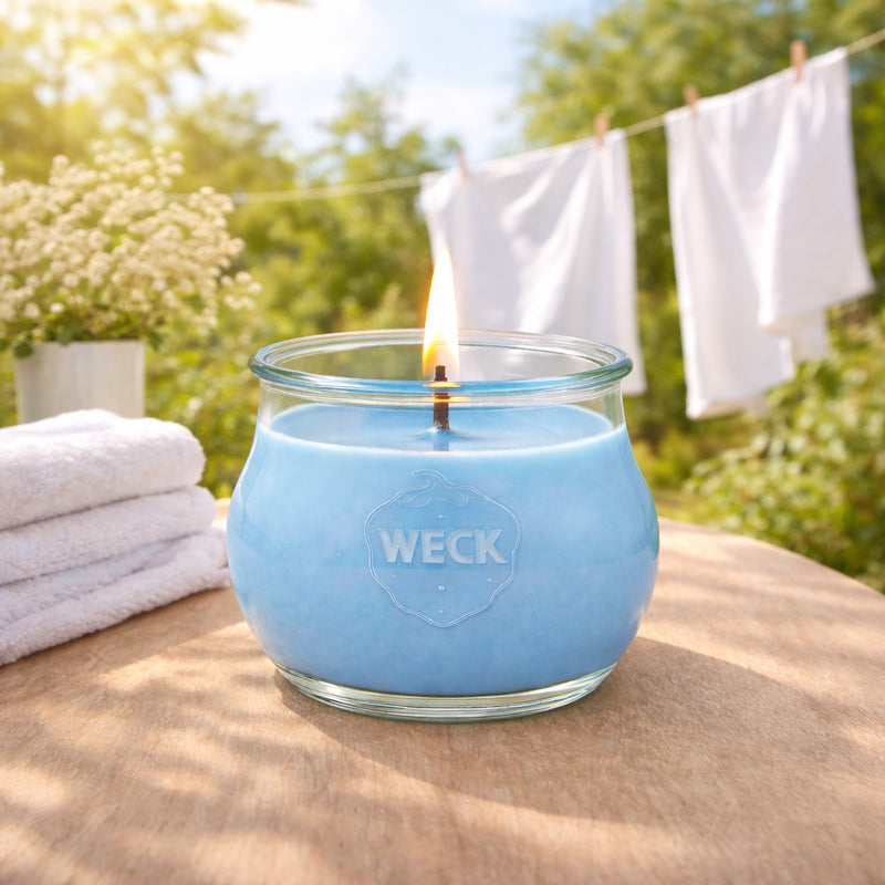 Große brennende blaue CandleDeko Duftkerze Frische Wäsche im WECK-Glas auf Gartentisch neben weißer Wäsche.