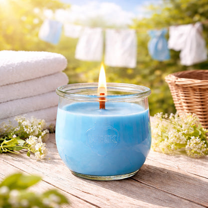 Brennende blue CandleDeko Frische Wäsche grosse Duftkerze aus pflanzlichem Kokoswachs im WECK-Tulpenglas neben weichen, weißen Handtüchern.