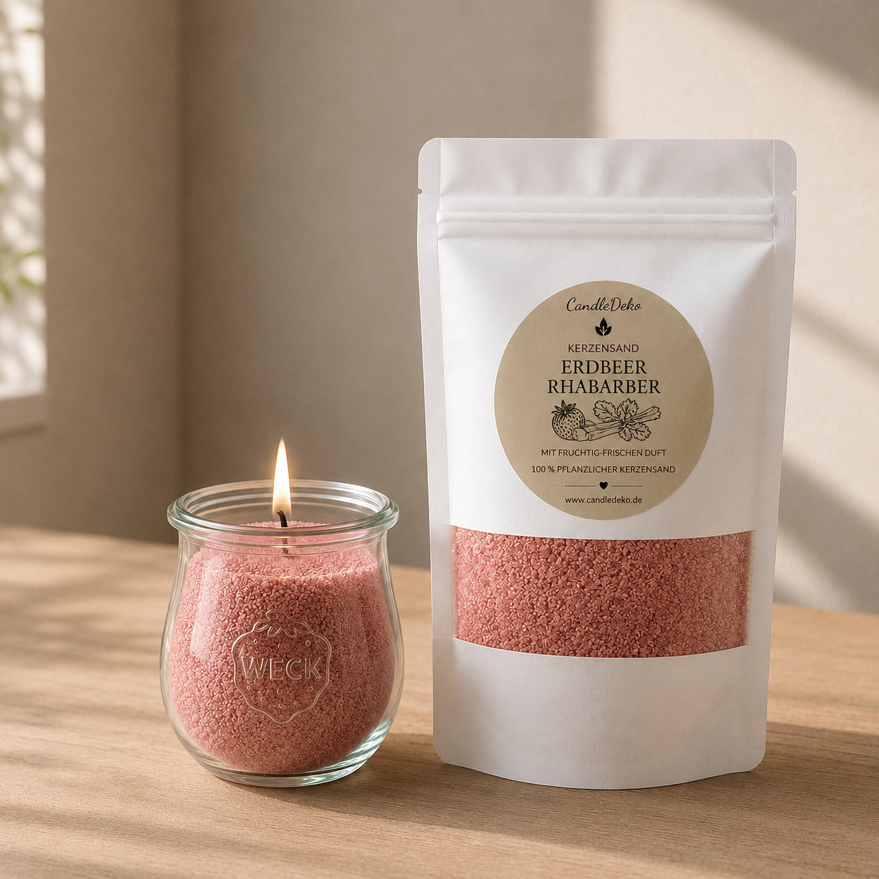 Ein weißer CandleDeko Nachfüllbeutel mit rosafarbenem Kerzensand Erdbeer Rhabarber neben einer brennenden Kerze im bauchigen WECK-Glas auf einem hellen Holztisch.