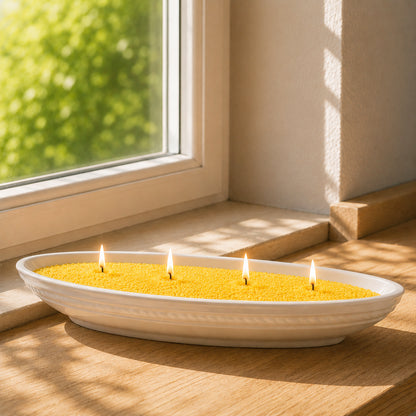 Gelber CandleDeko Kerzensand brennt mit vier Dochten in einer weißen, bootsförmigen Kerzenschale aus Keramik auf einer hölzernen Fensterbank im Sonnenlicht.