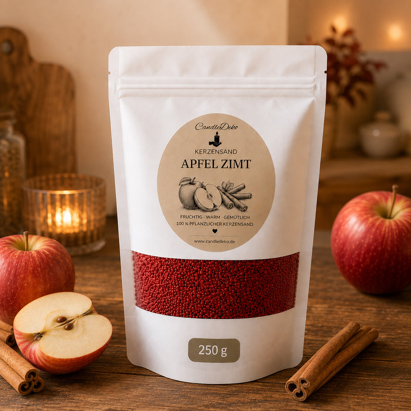 Ein weißer CandleDeko Standbodenbeutel mit 250g dunkelrotem Kerzensand Apfel Zimt auf einem Holztisch neben frischen Äpfeln im Korb und Zimtstangen.