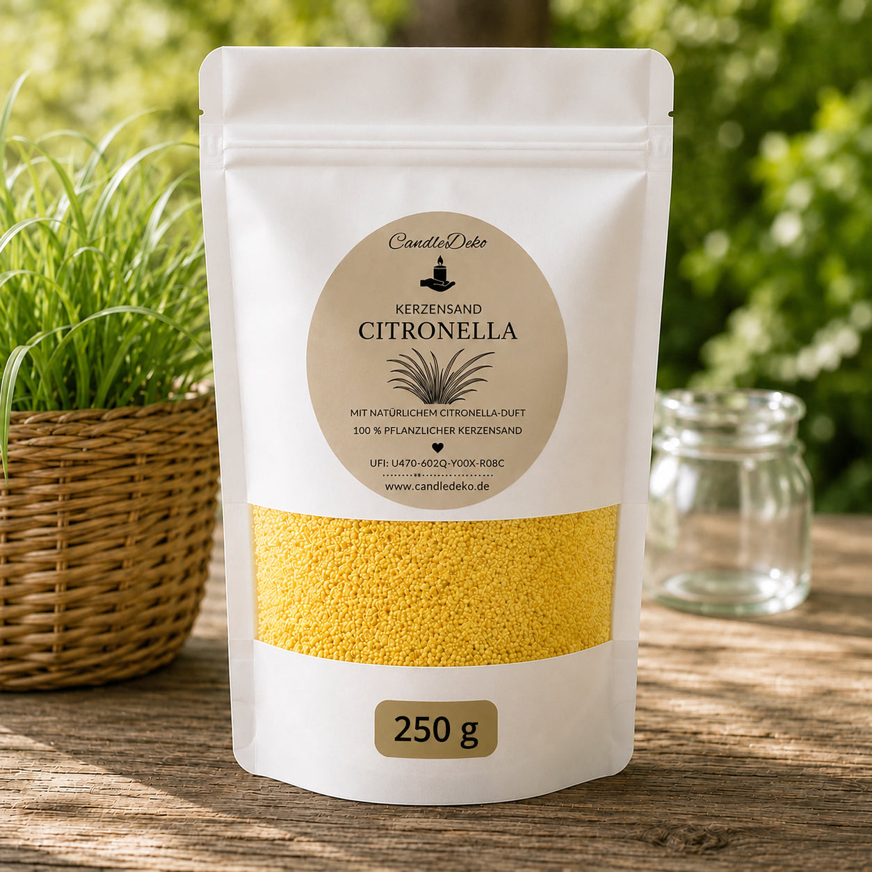 Ein weißer CandleDeko Standbodenbeutel mit 250 g gelbem Kerzensand Citronella auf einem rustikalen Holztisch neben einem geflochtenen Gras-Übertopf im Freien.