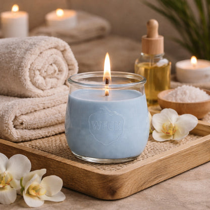 Große Spa Ritual Duftkerze aus Kokoswachs im WECK-Tulpenglas neben flauschigen Handtüchern und Öl.
