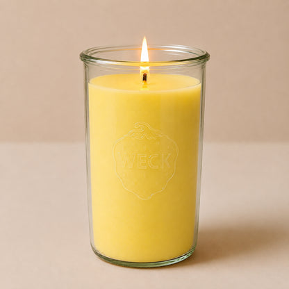 Brennende warm-gelbe CandleDeko XXL Duftkerze im hohen WECK-Sturzglas vor neutralem Hintergrund