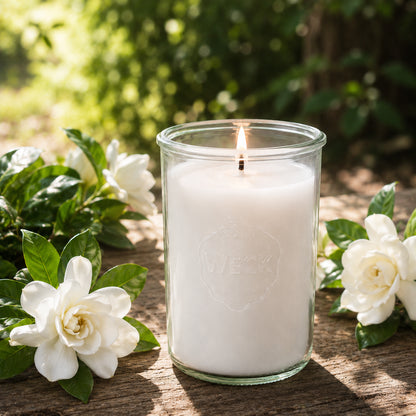 rennende weiße CandleDeko XXL Duftkerze im WECK-Sturzglas auf Holzplatte neben frischen Gardenienblüten.